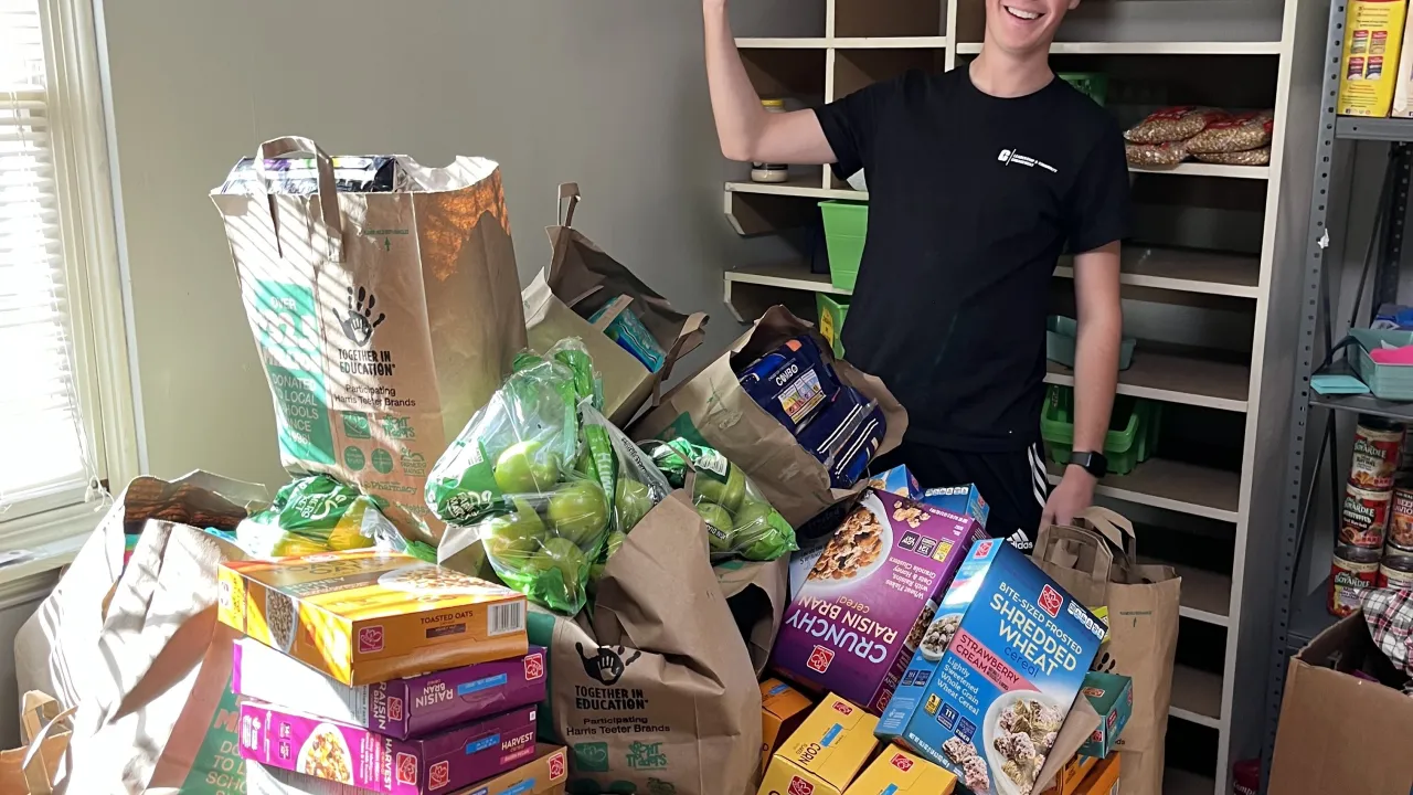 Matthew McGrew smiling behind a load of groceries at the Jamil Niner Student Pantry