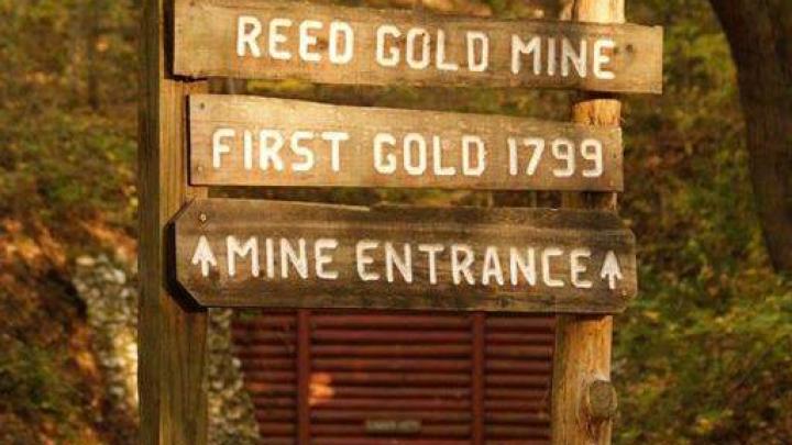 Sign post for Reed Gold Mine reads "Reed Gold Mine First Gold 1799 Mine Entrance"