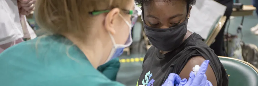A masked student sitting down getting a vaccine shot