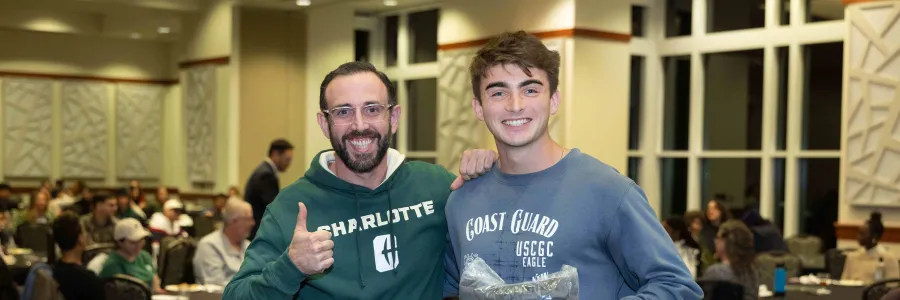 Two men posing with a giveaway from the Military & Veteran Services welcome back dinner