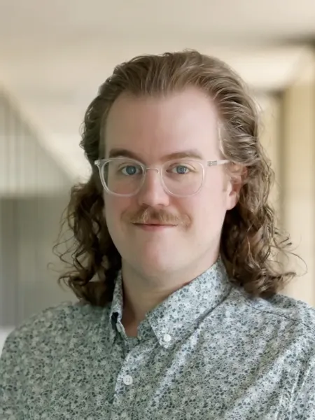 Mark Manning grinning with a button up shirt on in a hallway