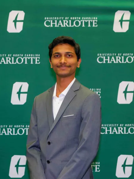 Ajay Divakar Sudhir smiling in front of a UNC Charlotte backdrop