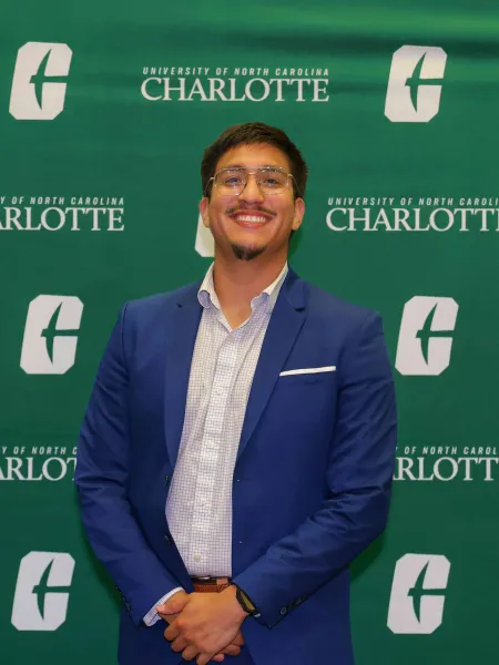 Christopher Ortega Saavedra smiling in front of the UNC Charlotte backdrop