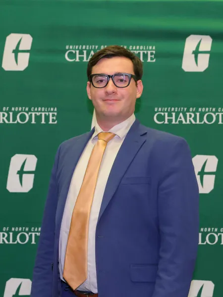 Isaiah Grayson in a suit and tie in front of a UNC Charlotte backdrop