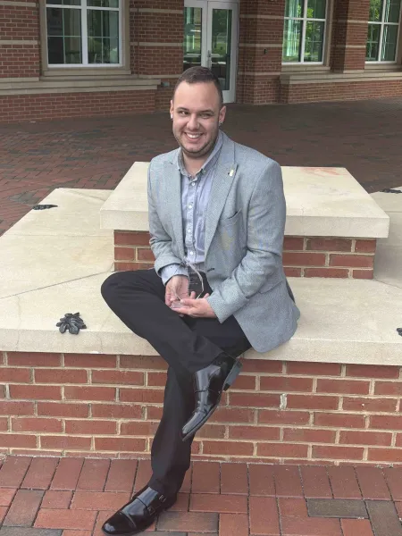 Milan Novakovic sitting down in a suit holding his Student Affairs award