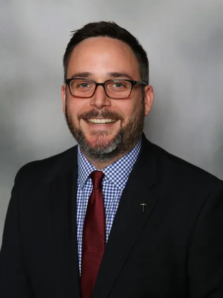 Paul Holliday-Millard smiling in a suit and tie.