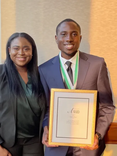 Caleb Achidi smiling while holding his Derrick Griffith Servant Leadership Award