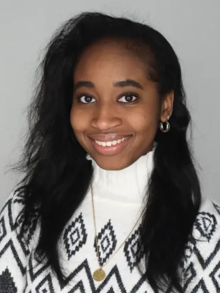 Pennda Arami smiling with a gray background in a white sweater