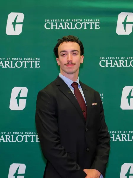 Zack Lowell smiling in front of the UNC Charlotte backdrop