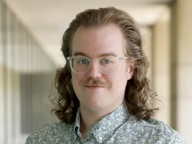 Mark Manning grinning with a button up shirt on in a hallway