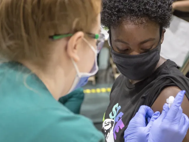 A masked student sitting down getting a vaccine shot