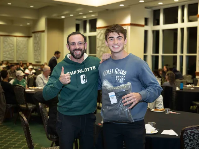 Two men posing with a giveaway from the Military & Veteran Services welcome back dinner