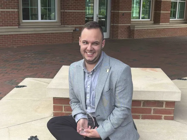 Milan Novakovic sitting down in a suit holding his Student Affairs award
