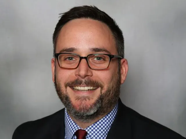 Paul Holliday-Millard smiling in a suit and tie.