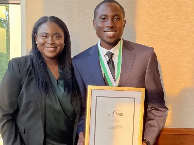 Caleb Achidi smiling while holding his Derrick Griffith Servant Leadership Award