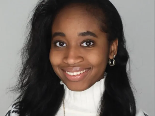 Pennda Arami smiling with a gray background in a white sweater
