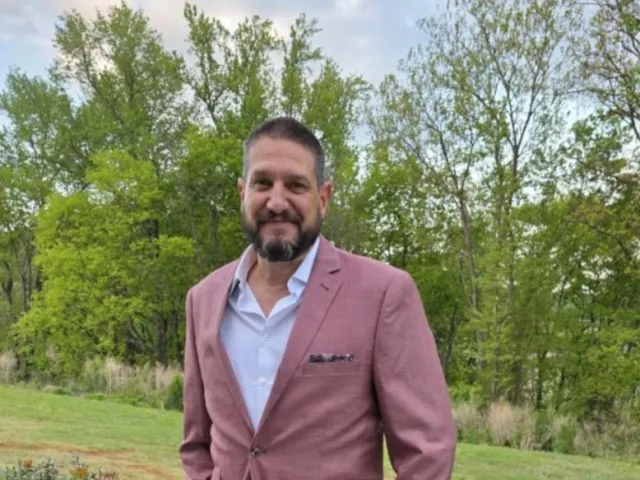 Steven Begley in a salmon-colored suit posing outside
