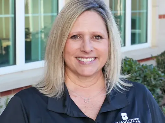 Wendy Moore smiling in front of a building in a black Housing and Residence Life polo shirt