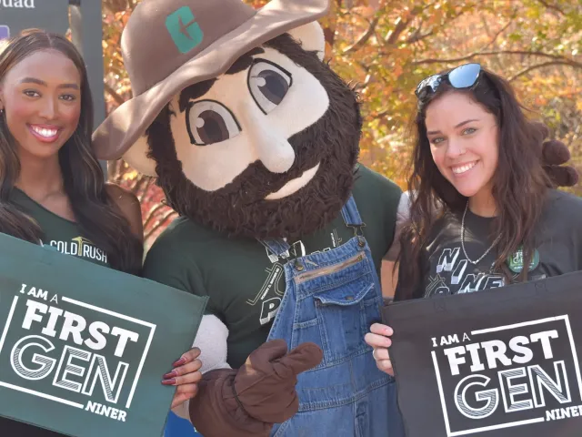 Two students standing by Norm with First Gen signs