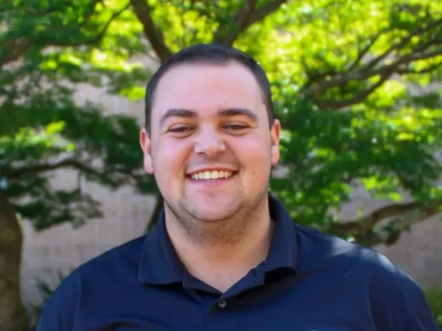 Lance Bumgardner smiling in a black polo with the All In C