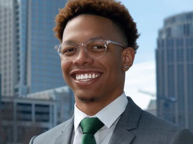 Shaun Coleman smiling in front of a city with a green tie.