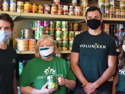 Four people standing in front of food cans at the Student Pantry.