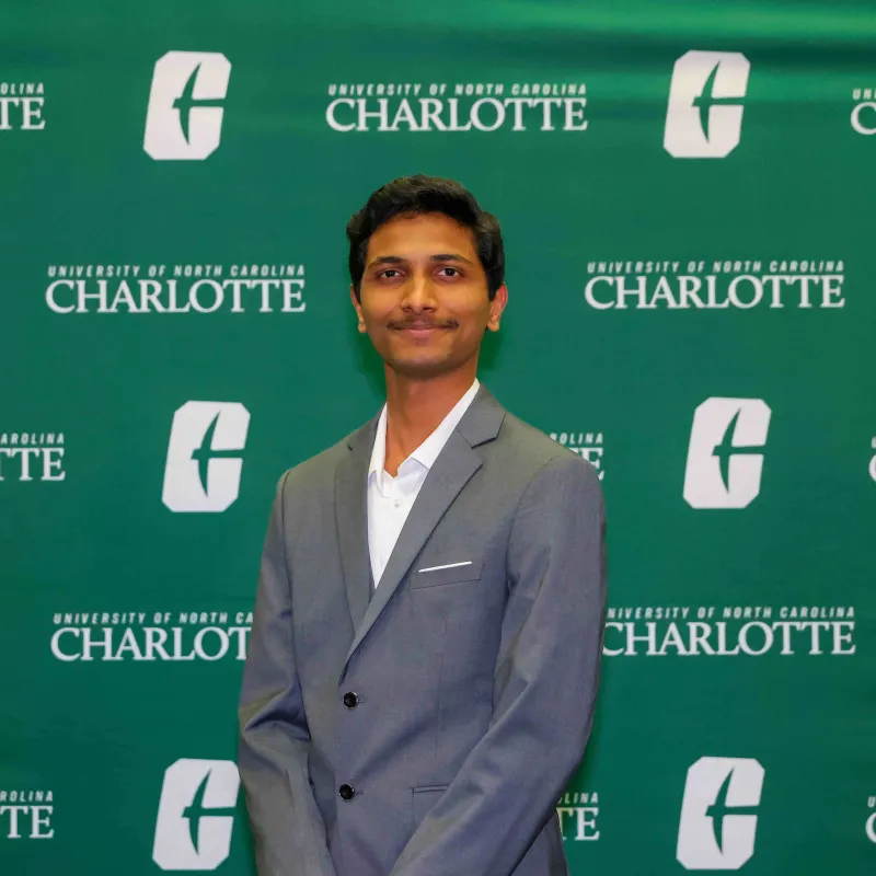 Ajay Divakar Sudhir smiling in front of a UNC Charlotte backdrop