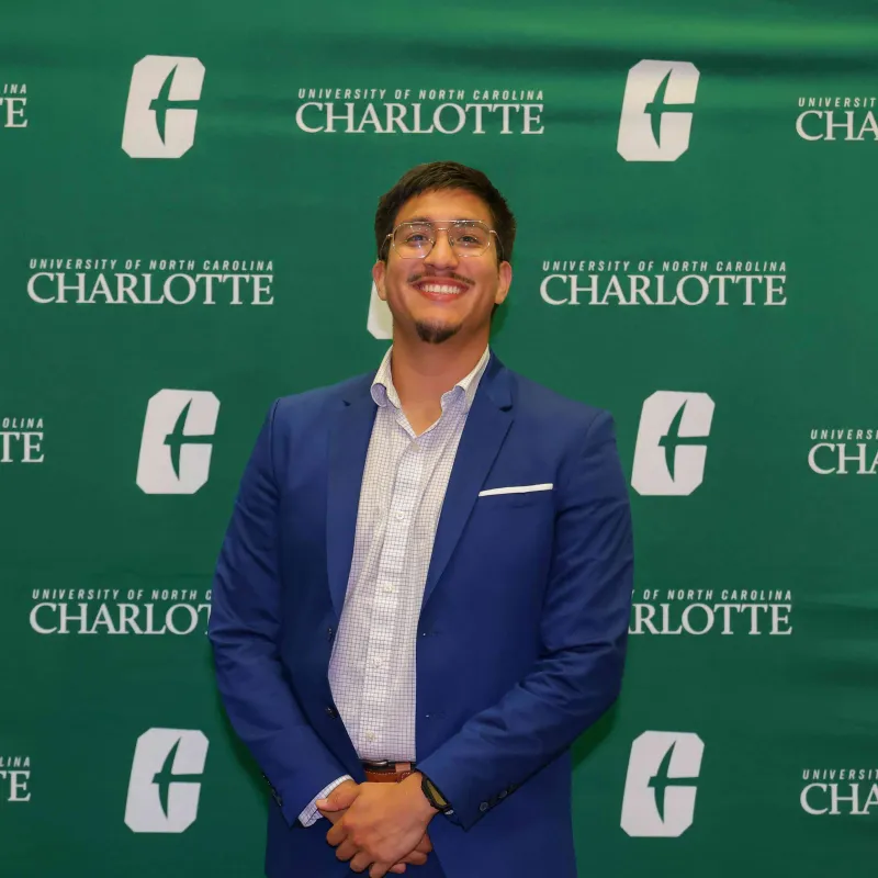 Christopher Ortega Saavedra smiling in front of the UNC Charlotte backdrop