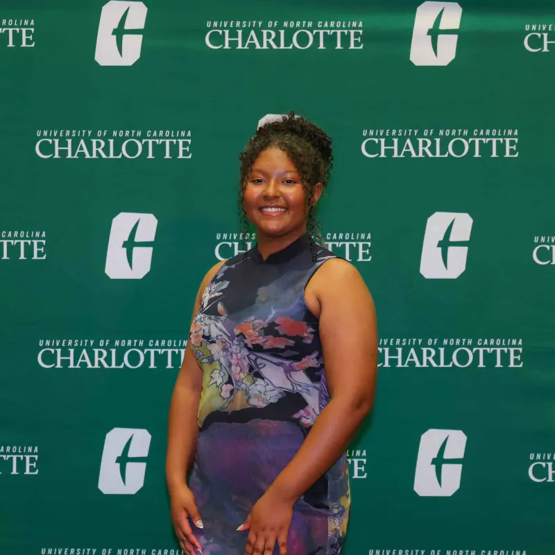 Daphne-Lorraine Chinfloo smiling in front of the UNC Charlotte backdrop