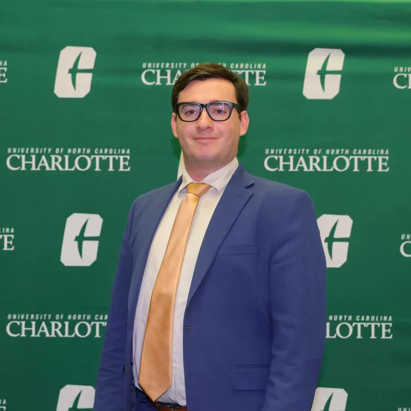 Isaiah Grayson in a suit and tie in front of a UNC Charlotte backdrop