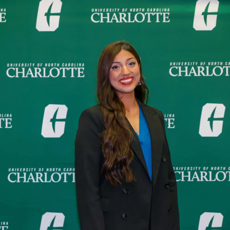 Noorkaran Chima smiling in front of a UNC Charlotte backdrop