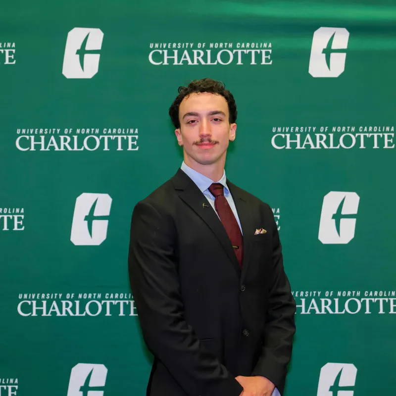 Zack Lowell smiling in front of the UNC Charlotte backdrop